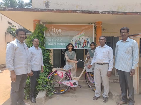 Six people standing in front of a building with a bicycle, posing for a group photo